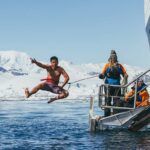Polar plunge - Man leaps off gangway of ship above blue ocean water with snow covered coastline background. Travel Antarctica Travel Polar