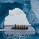 Zodiac boat with passengers are seen through a hole in a massive white and blue iceberg. Cruise holiday Antarctica Travel holiday Antarctica
