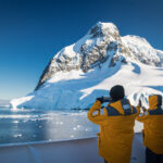 Passengers aboard cruise ship view mountain glacier in the Lemaire Channel Antarctica. Small bergy bits of ice can be seen in the water. Cruise Antarctica Antarctica holiday