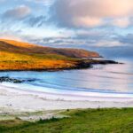 Green and yellow hill sides along the white sand beach and blue sea water in Easter Island. Travel Easter Island