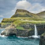 Waterfall cascading off cliff edge into ocean at the Faroe Islands. Scottish Island cruise