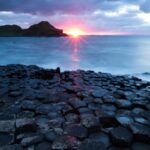 Flattened rocks of Giant's Causeway under the light of the setting sun. Cliffs of Skellig Islands rising out of the dark blue in the Celtic / Irish Sea. Sea cruise Celtic / Irish Sea.