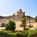 Aswan keep on hill above the river bank of The Nile. River leads to lush green bank and then sandy hill which atop sits the stone keep. Nile River Cruise in Egypt Africa.