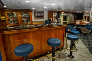 Main lounge bar of the Ocean Adventurer ship designed for cruising the Arctic and Antarctic regions. Classic wooden bar with blue bar stools.
