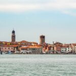 Distant view of Chioggia City Italy from the sea. Plenty of sailing boats litter the banks with the old buildings behind. Venice Cruise - Italy