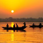 Sunset on the Ganges river India with local row boats in foreground and jungle river bank in the background. The golden light of the sunset creates silhouettes of the aforementioned. India river trip - Ganges River