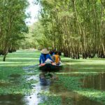 Local Vietnamese on a small boat among the jungle trees of the Meekong Delta. Paddling over green water plants. Asian river cruise - river trip.