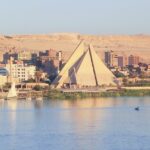 Minya city Egypt from the Nile River. Scenery of the river in foreground with local fishing boats on the bank, the intriguing architecture of the city and then the dry dessert sand hills further behind. Nile river cruise