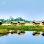 Raised wooden village huts on bank of river with jungle in far background. Mishing Village along the Brahmaputra River. India River Cruise.