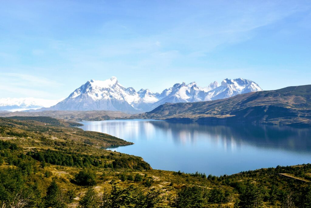 Stunning view of a lake nestled the green hills and ice capped mountains in the background in the Patagonian region of South America. Small group tours.