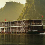 River cruise ship Angkor Pandaw, cruising along glassy water of the river with majestic jungle covered mountain peaks on the banks of the river.