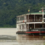 River cruise ship Katha Pandaw on the Ganges River India. Classic 2 deck ship moored on bank of river with the jungle flora in the background. Asian river trip.