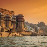Varanasi city view. Ancient Indian city with stone steps onto the river with stone buildings behind. River cruise Ganges River India.