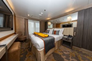 A view of the Polar expedition ship - World Explorer's Deluxe Suite. Two twin beds together to form a double bed with classy linen and pillows, face a large TV screen. Wooden fixtures finish off the cabin.