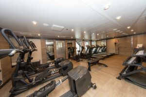 Gym of the World Explorer ship. Sleek wooden flooring and mirrored walls create a sense of space for the gym equipment comprising of treadmills, weights and stair climbers.